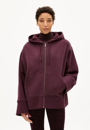 Bordeauxfarbener Kapuzenpullover mit Reißverschluss, großen Fronttaschen und weiten Ärmeln, kombiniert mit schwarzen Leggings mit einem Zebra-Design.