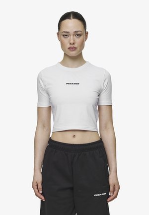 White cropped t-shirt with short sleeves, featuring a black logo "PEGADOR" on the chest, paired with black elastic waistband pants.