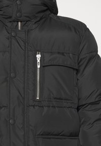 Černá péřová bunda s kapsou na zip na hrudi, patentkami a vysokým límcem. Vyrobena z hladkého, lesklého materiálu s prošívanou texturou.