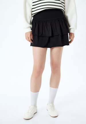 Zwarte gelaagde rok met een gerimpeld ontwerp, zachte stof, elastische tailleband, gecombineerd met witte sneakers en kniehooge sokken.