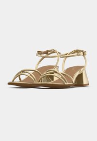 Sandale cu toc auriu, cu multiple curele subțiri, toc bloc triunghiular și branț bej. Finisaj metalic neted, cu detalii minimale.
