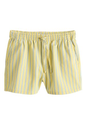 Personne portant un short jaune à rayures bleues verticales avec un cordon noué, associé à un crop top blanc texturé.