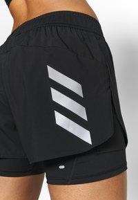 Svarta sportshorts med en silverfärgad geometrisk design på sidan, tillverkade av lätt, mjukt material med elastisk midja.