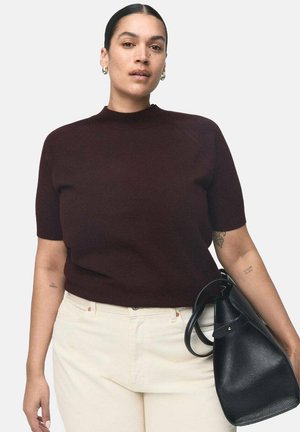 Suéter de punto burdeos de manga corta con cuello alto; combinado con pantalones color crema y sosteniendo un bolso de cuero negro.