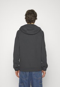 Dunkelgrauer Hoodie mit geräumiger Kapuze, gerippten Bündchen und Saum. Weicher Stoff mit flachen Nähten für einen sauberen Abschluss. Lässige Passform.
