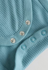 Himmelblaues geripptes Material mit silbernen Druckknöpfen und blauen Kunststoffverschlüssen entlang des Ausschnitts und des unteren Randes. Glatte Textur.