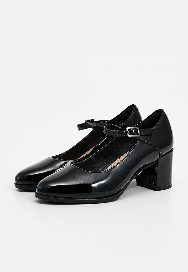 Schwarze Lackleder-Mary-Jane-Schuhe mit runder Spitze, einem Schnallenriemen um den Knöchel und einem Blockabsatz. Glatte Textur.
