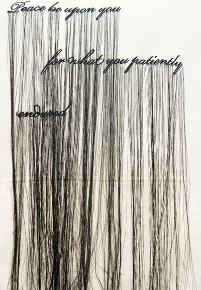 Nežna črna nit, ki tvori besede »Mir naj bo s teboj za tisto, kar si potrpežljivo prenesel«, z dolgimi nitmi, ki visijo navpično.