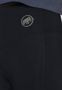 Zwarte sportleggingen met een grijs mammoetlogo en contrasterende stiksels. Het materiaal is glad met een aansluitend ontwerp.