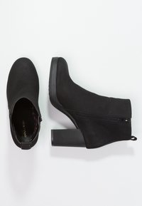 Botines negros de ante con cierre de cremallera en el lado exterior y un tacón cuadrado texturizado. Superficie suave y diseño de punta redondeada.