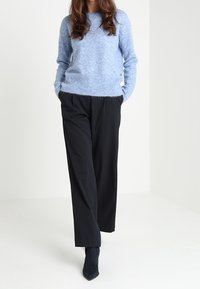 Ljusblå, strukturerad tröja med rund halsringning, kombinerad med svarta, löst sittande byxor och mörka ankelstövlar. Enkel, minimalistisk design.