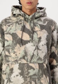Felpa con cappuccio realizzata in pile testurizzato con un motivo camouflage in verde spento, beige e grigio. Presenta una tasca frontale e cordini.