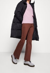 Svart puffjacka, ljusrosa stickad tröja, bruna utsvängda byxor och grå snörskor med tjock sula. Rent, strukturerade linjer.