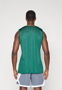 Zelený športový top z jemného materiálu s okrúhlym výstrihom, bez rukávov a vo voľnom strihu, v kombinácii so šedými šortkami s bielymi akcentmi.