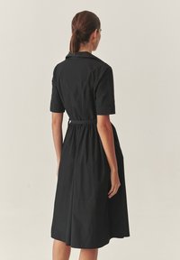 Čierne, krátke šaty s golierovým výstrihom a zúženým pásom, s voľnou sukňou, ktorá končí tesne pod kolenami.