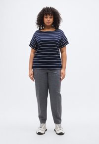 Ριγέ πουκάμισο σε ναυτικό μπλε με κοντά μανίκια, σε συνδυασμό με γκρι παντελόνι κομμένο στο μέτρο. Το σύνολο ολοκληρώνεται με λευκά και μαύρα αθλητικά παπούτσια.