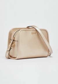 Bolso de cuero dorado con textura, cierre de cremallera y correa ajustable, con un logotipo de la marca en el frente y forma rectangular.