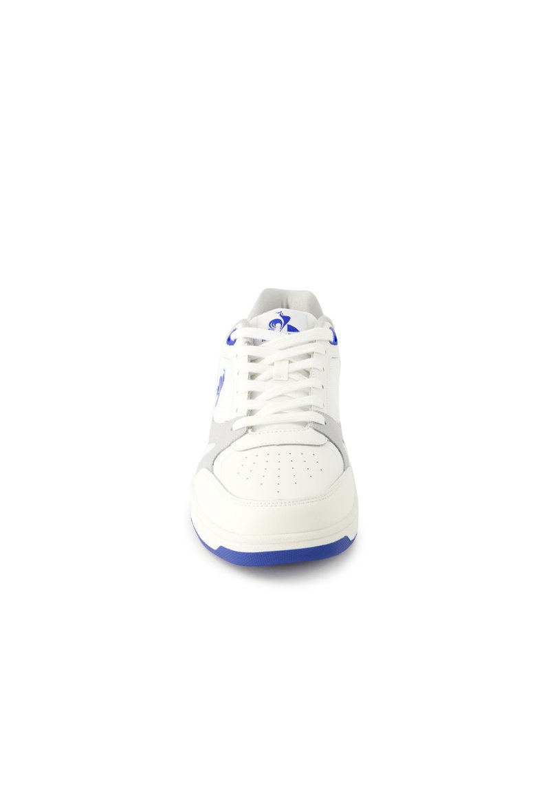 Sneaker blanche avec des accents gris, des éléments en bleu et un embout perforé. Design minimaliste avec des lacets plats et une semelle ronde.