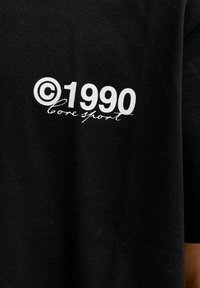 Czarny bawełniany t-shirt z białym napisem: „©1990 core sport”, o gładkiej fakturze i krótkich rękawach.