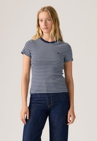 Marineblauw-wit gestreept T-shirt met een ronde hals, korte mouwen, aangesloten pasvorm en een klein logo op de borst. Draagt bijpassende donkere denim jeans.