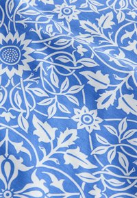 Tejido de algodón con fondo azul y patrones florales y de hojas en blanco, con detalles intrincados y una textura suave.
