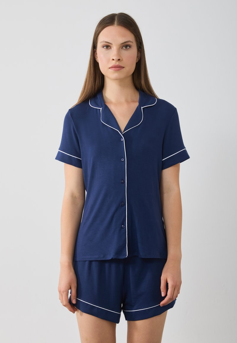 Marineblå pyjamasset i mjukt tyg, med kortärmad skjorta med knappar och matchande shorts med vit kant.
