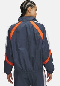 Navy windbreaker with orange and white accent stripes, lightweight fabric, elastic cuffs, and waistband, featuring a high collar design.