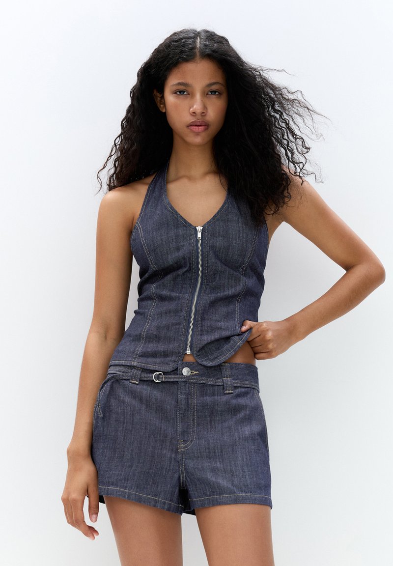 Denim haltertop med dragkedja fram och figurnära design, ihop med mörka denimshorts med bälte i midjan och kontrasterande sömmar.