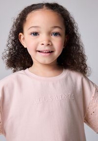 Top de manga corta en color rosa claro con un ajuste holgado, logo bordado "ALLSAINTS" y detalles de encaje estampado en las mangas.