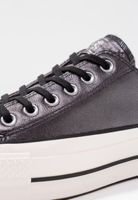 Svart snörsko med metallgrå ovandel, rund tå, silverfärgade öglor, texturerad yta och en vit gummisula med svart rand.