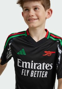 Svart fotbollströja med korta ärmar. Har gröna och röda randiga detaljer, vit text "Emirates FLY BETTER" och en röd klubblogotyp på bröstet.