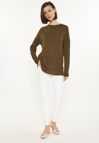 Olivegrünes, geripptes Langarmshirt mit drei Knöpfen, kombiniert mit weißen, schlanken Hosen und hellen Ballerinas. Einfaches Design und lockere Passform.