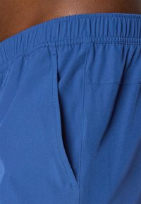 Blå svøm shorts med elastisk talje, sidelommer og glat tekstur. Har ren syning og et enkelt design.