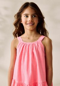 Vestido de algodón rosa con tirantes anchos, recogido en el escote, que presenta un cuerpo fluido y un dobladillo en capas. Textura suave, diseño ligero.