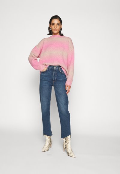 Maglione a maglia con gradiente da rosa a beige, con collo a giro, abbinato a jeans dritti blu e stivali alla caviglia bianchi in pelle di serpente.
