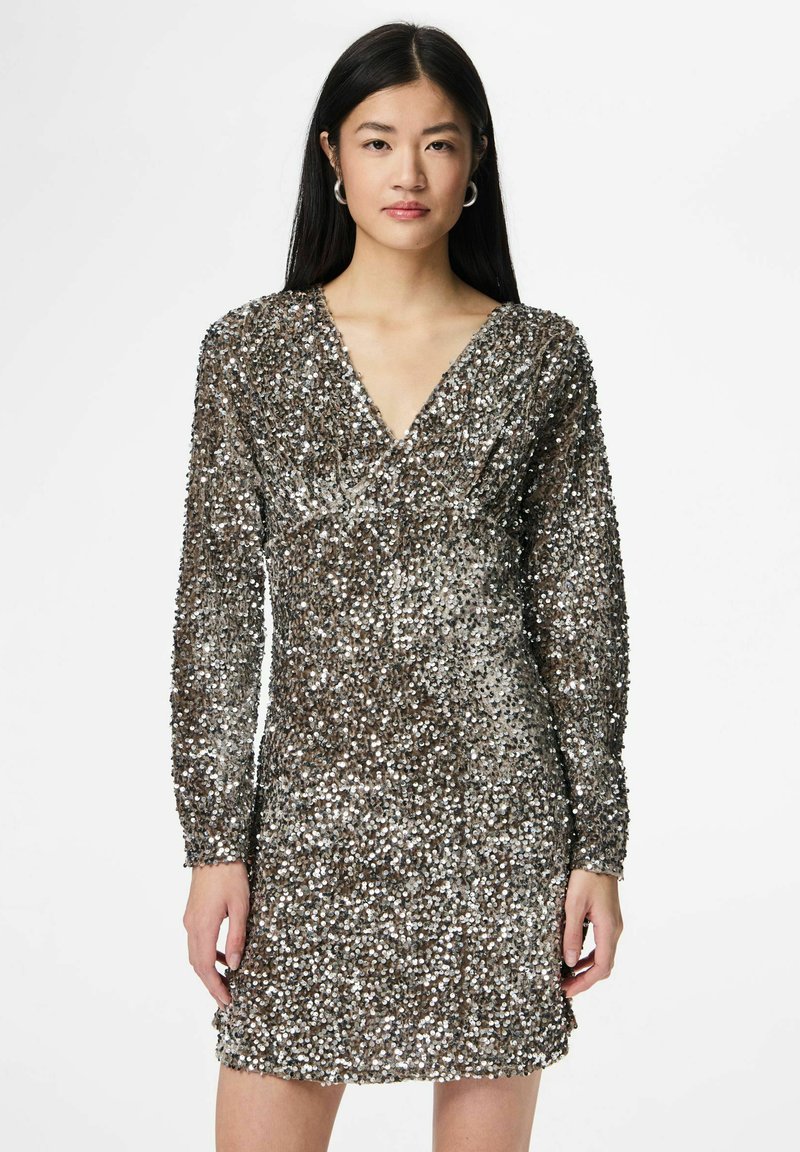 Vakarinė suknelė su ilgomis rankovėmis, V formos iškirpte ir aptempta silueto linija. Sukurta iš sidabro ir rudos spalvų derinio su blizgiu paviršiumi.