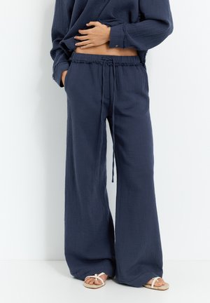 Navyblauwe wijde broek van geweven stof met een koordjes taille. Gecombineerd met witte sandalen, wat zorgt voor een ontspannen silhouet.