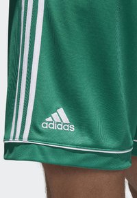 Pantaloni corti sportivi verdi realizzati in un tessuto morbido, con tre strisce bianche sui lati e un logo Adidas bianco ricamato vicino all'orlo.