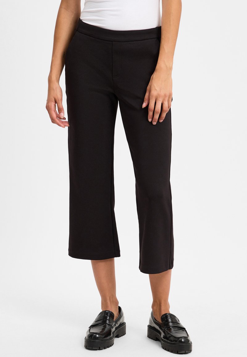 Black cropped pants made of stretchy fabric, featuring a smooth texture, elastic waistband, and a straight leg cut. Black footwear completes the look.