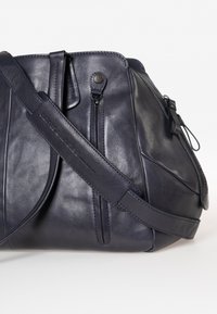 Borsa a tracolla in pelle blu scuro con una tasca con zip, texture liscia, cuciture dettagliate e una tracolla. Gli accessori includono una chiusura a scatto.