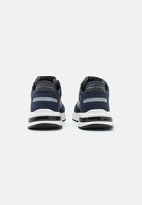 Baskets de sport bleu marine avec un dessus en textile lisse, des accents noirs contrastants, une semelle intermédiaire blanche rembourrée et un détail de logo sur le talon.