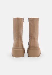 Botas de tobillo de piel marrón claro con una textura suave, que cuentan con un cierre de cremallera lateral y una suela de goma gruesa y texturizada.