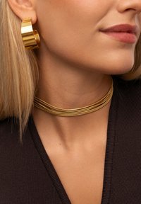Orecchini a cerchio dorati e collana choker in oro a strati. Gli orecchini hanno una finitura liscia e lucida; la collana è caratterizzata da più fili sottili intrecciati.
