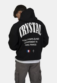 Felpa nera con grande scritta bianca "CRYSTAL" e testo aggiuntivo, con un piccolo dettaglio della bandiera francese sul retro.