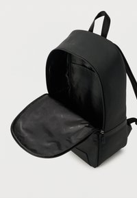 Μαύρο σακίδιο πλάτης με ανοιχτό το κύριο διαμέρισμα, που δείχνει το απαλό εσωτερικό επένδυμα και το φερμουάρ με γλωσσίδα κλεισίματος, πάνω σε απλό φόντο.