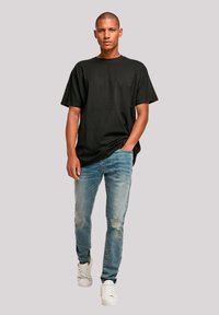 Schwarzes Baumwoll-T-Shirt mit lockerer Passform, kombiniert mit hellblauen, ausgewaschenen Jeans mit Rissen und weißen Turnschuhen.