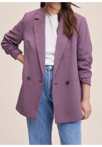 Blazer à motif pied-de-poule rose et noir avec une coupe cintrée, design à simple boutonnage, revers crantés, et accents de boutons, porté par-dessus un t-shirt blanc.