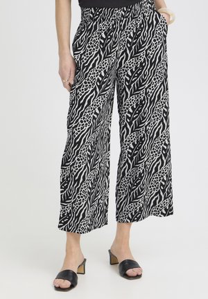 Čiernobiele nohavice s širokými nohavicami a abstraktným zvieracím vzorom, nosené s čiernymi otvorenými šľapkami na podpätku a čiernym topom.