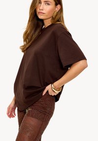 T-shirt marron à manches courtes en tissu doux, associé à des leggings marron à motifs et transparents ornés de décorations.