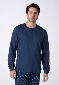 Maglietta henley a maniche lunghe blu navy con tre bottoni neri al collo, abbinata a pantaloni del pigiama con motivi a fantasia in blu chiaro.